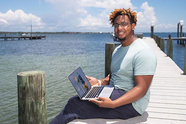 一名UWF学生坐在码头上使用笔记本电脑时面带微笑.